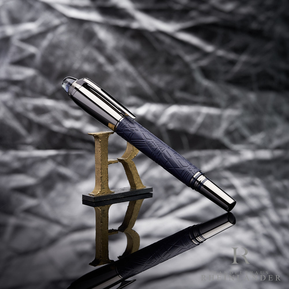 Silber- und blauer Rollerball an 3D-Buchstabe R lehnend vor grauem Knitteroptik-Hintergrund fotografiert