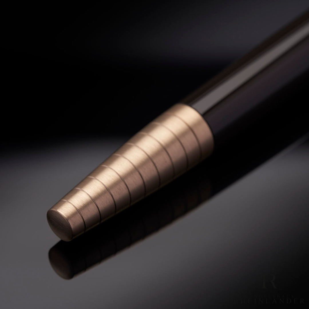 goldener Konus mit gebürstetem Finish und Rillenmuster des Montblanc Carlo Collodi Rollerballs auf schwarzem Tisch liegend