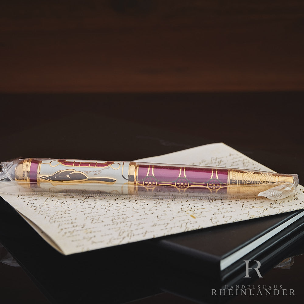 Rollerball Stift von Montblanc in rot, weiß, gold mit Clip in Form eines Blattes liegt auf einem Notizbuch